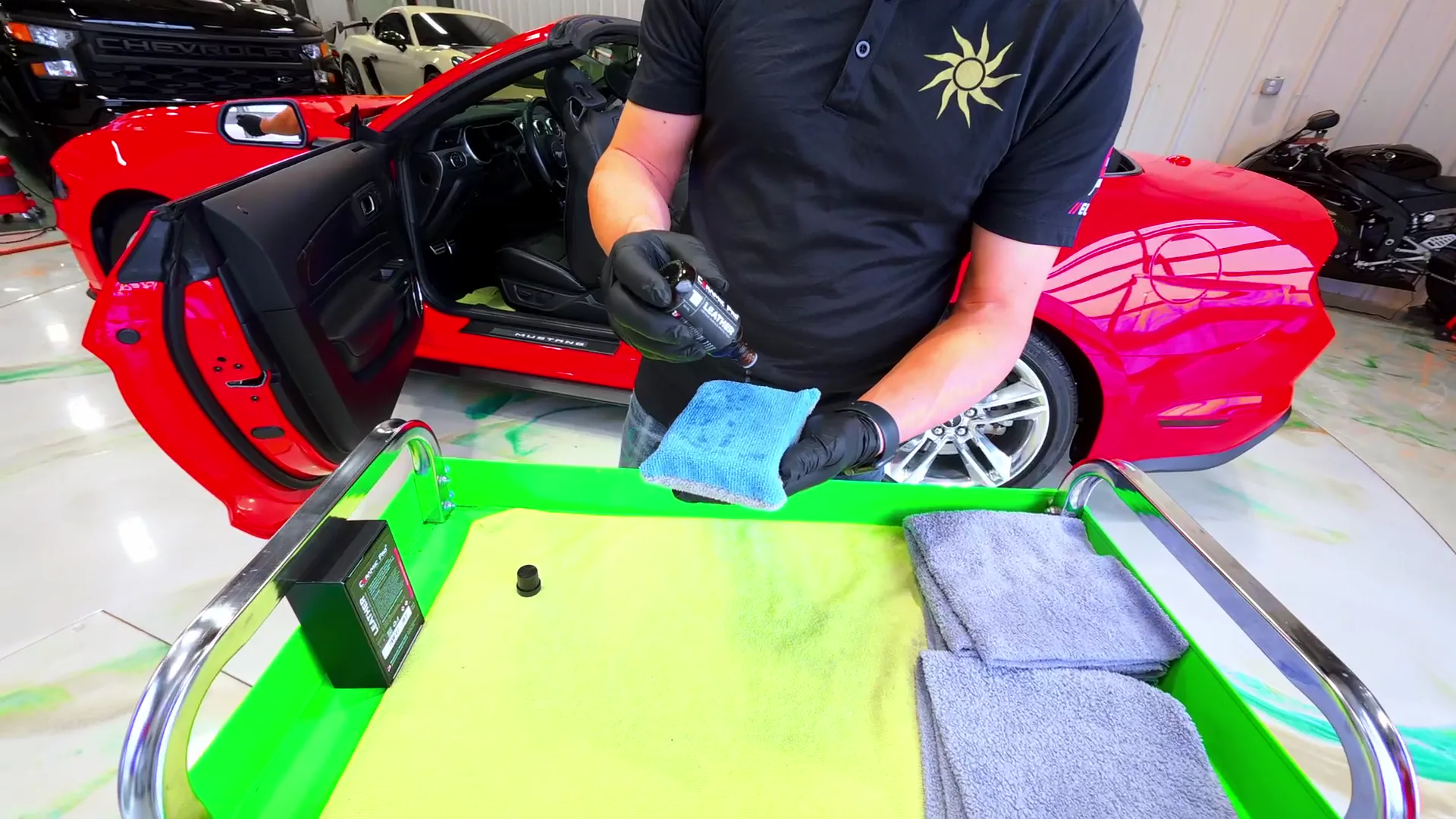 A technician in a Castro Oasis sun logo shirt working a red Mustang convertible, applicator pad and microfibre on a green cart.