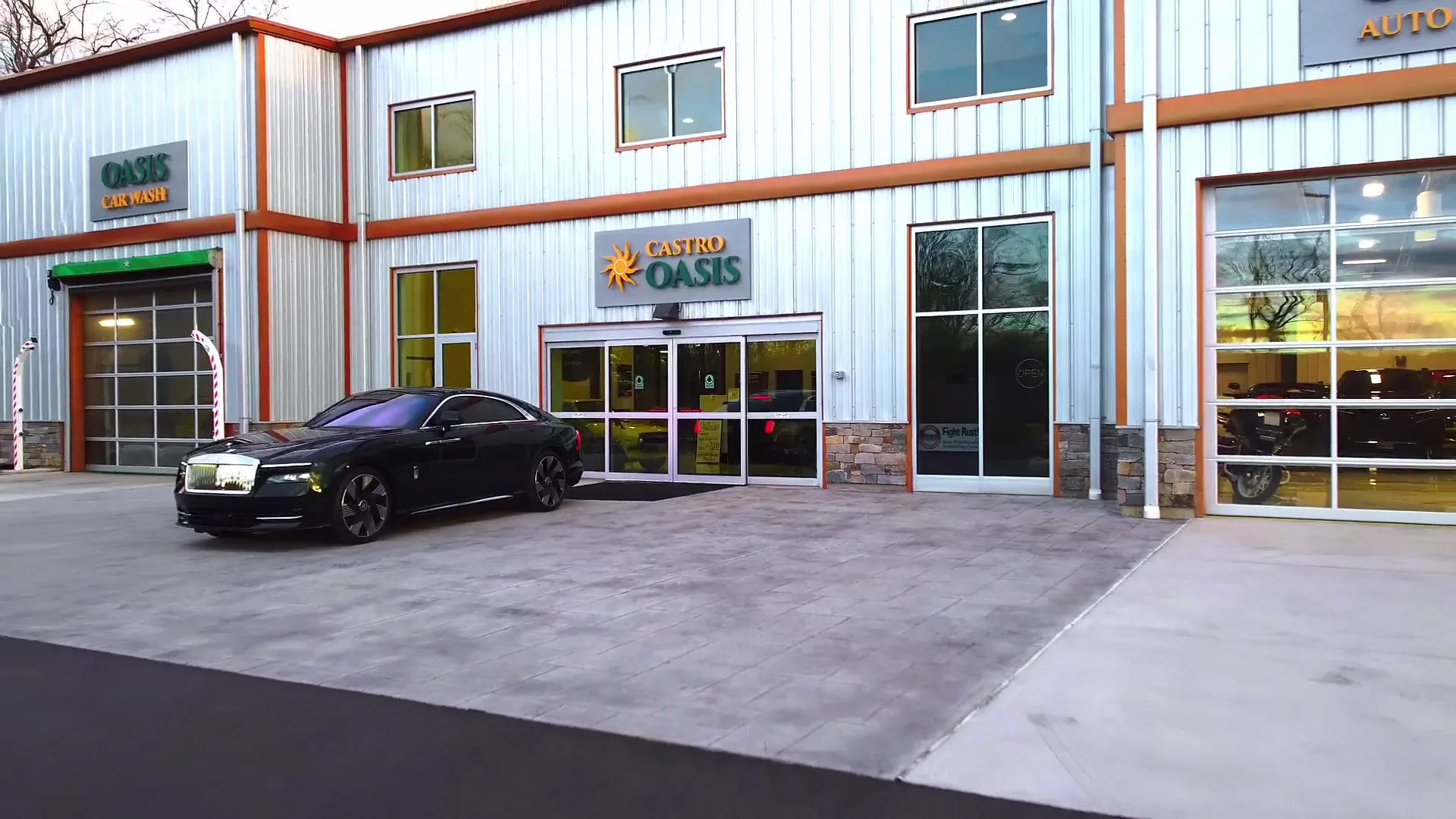 A black Rolls-Royce parked at the main doors of Castro Oasis, with the car wash bay on the left.