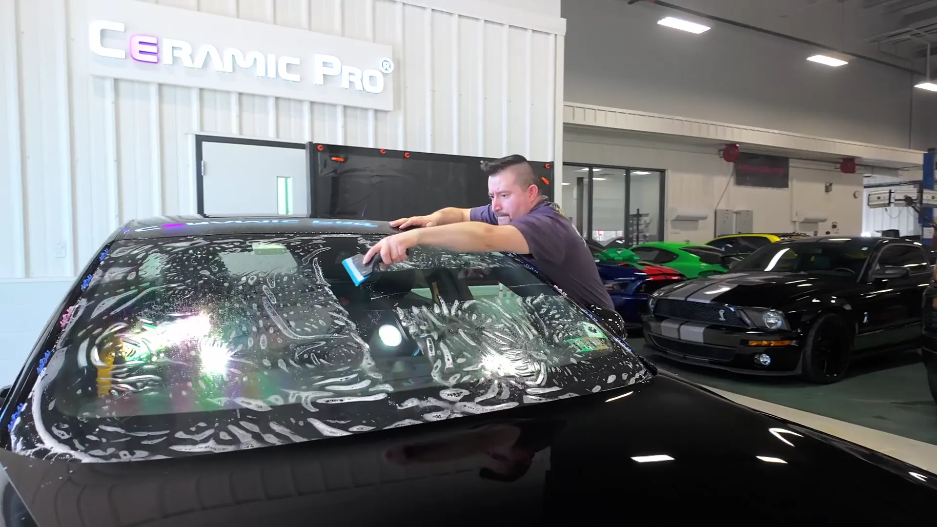 A technician working on a windshield with Ceramic Pro signage behind.