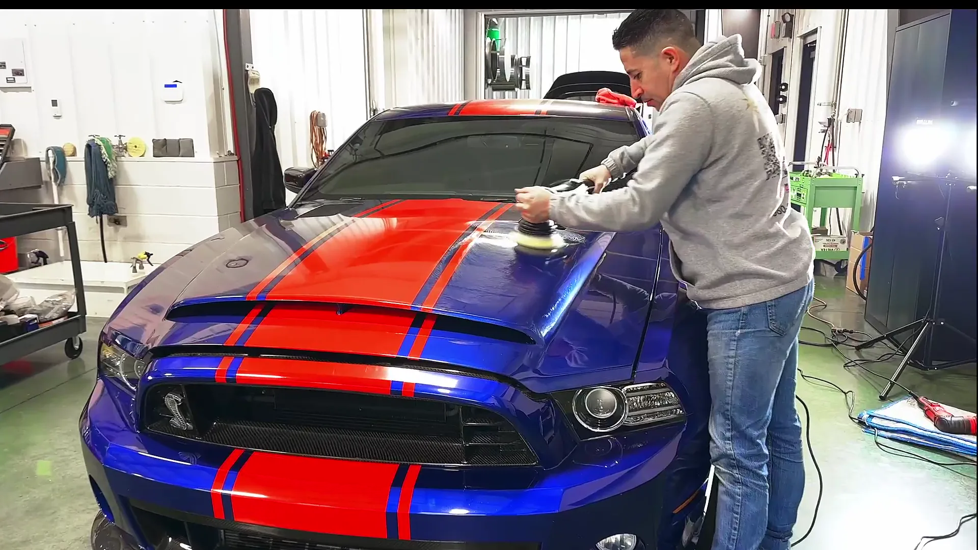 A technician machine polishing the hood of a blue Shelby with red stripes.
