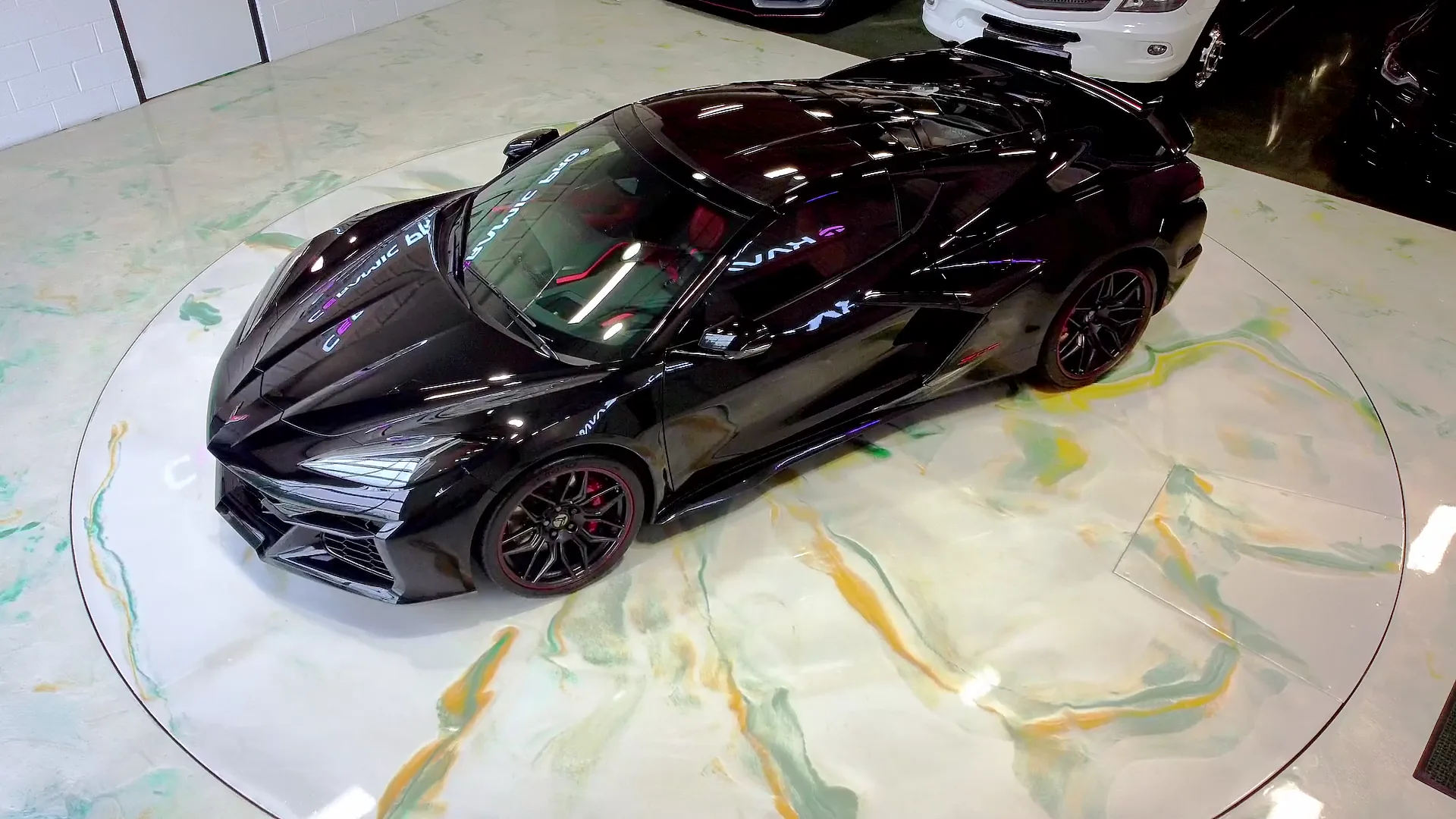 A black supercar on a lit turntable on a marbled floor.