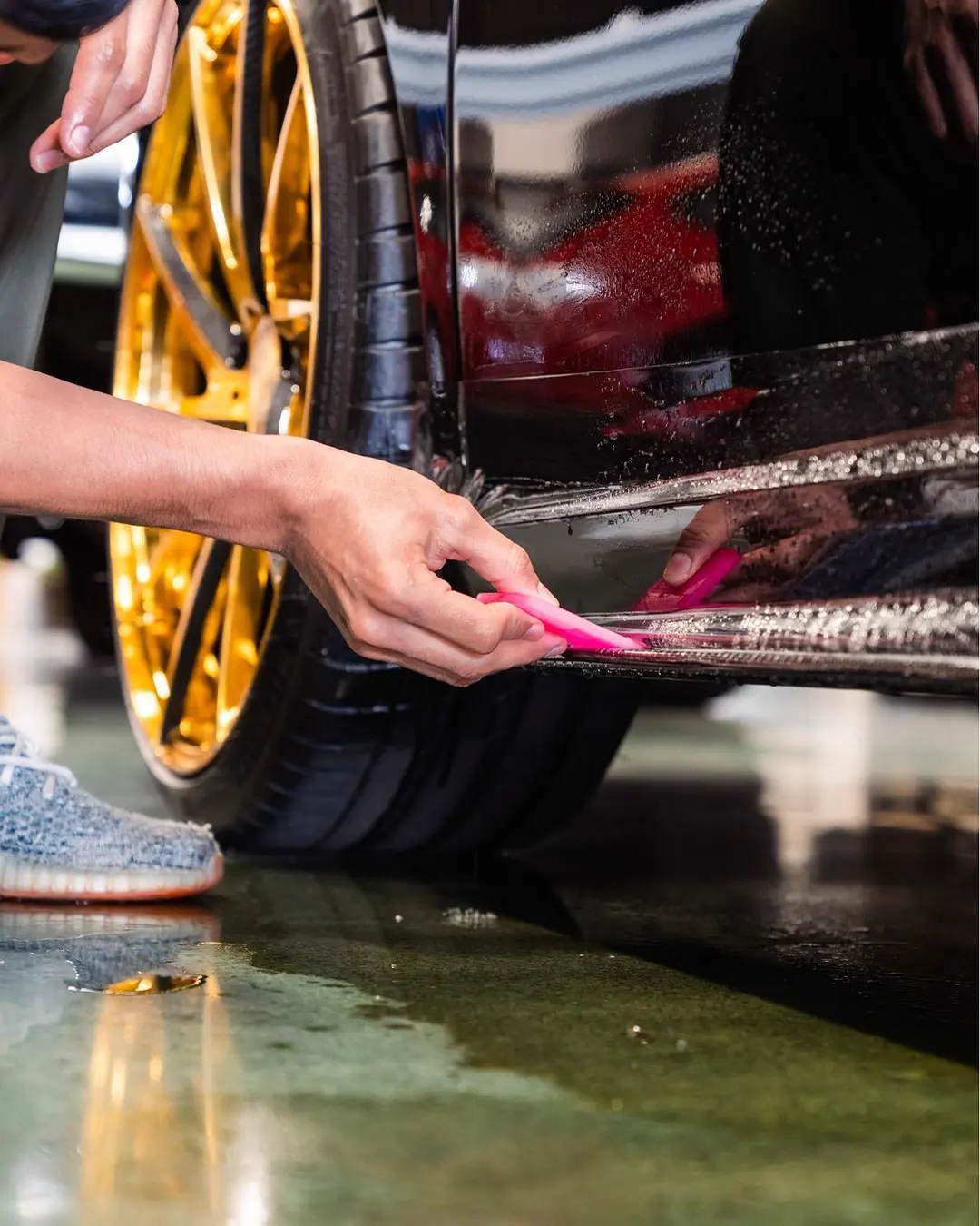 Gloved hands squeegeeing paint protection film along the rocker of a Lamborghini Gallardo.